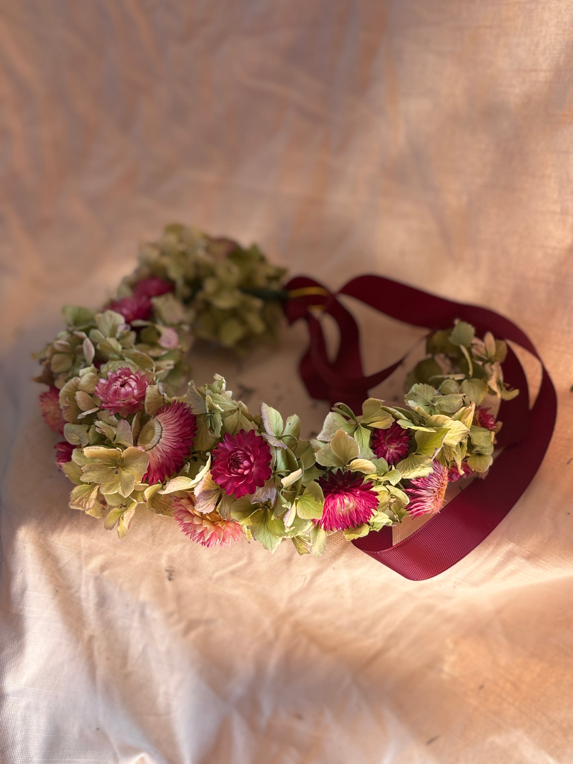 Dried flower crown with pink and green flowers on a textured beige background