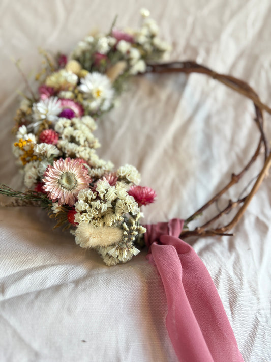 Floral wreath with dried flowers and a pink ribbon on a white fabric background