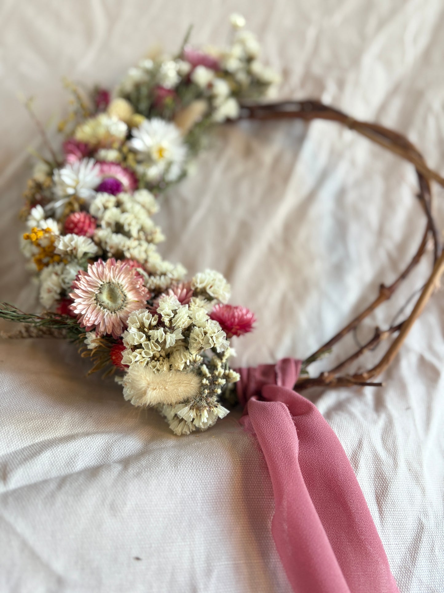 Floral wreath with dried flowers and a pink ribbon on a white fabric background