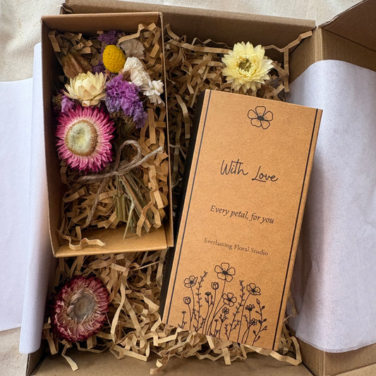 Box of dried flowers with a card labeled 'With Love' on a neutral background