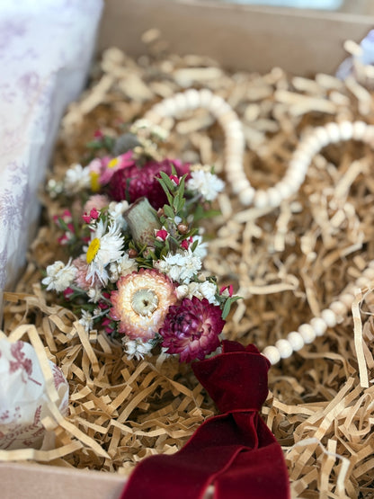 Small bouquet of dried flowers in a box with shredded paper and a red ribbon.