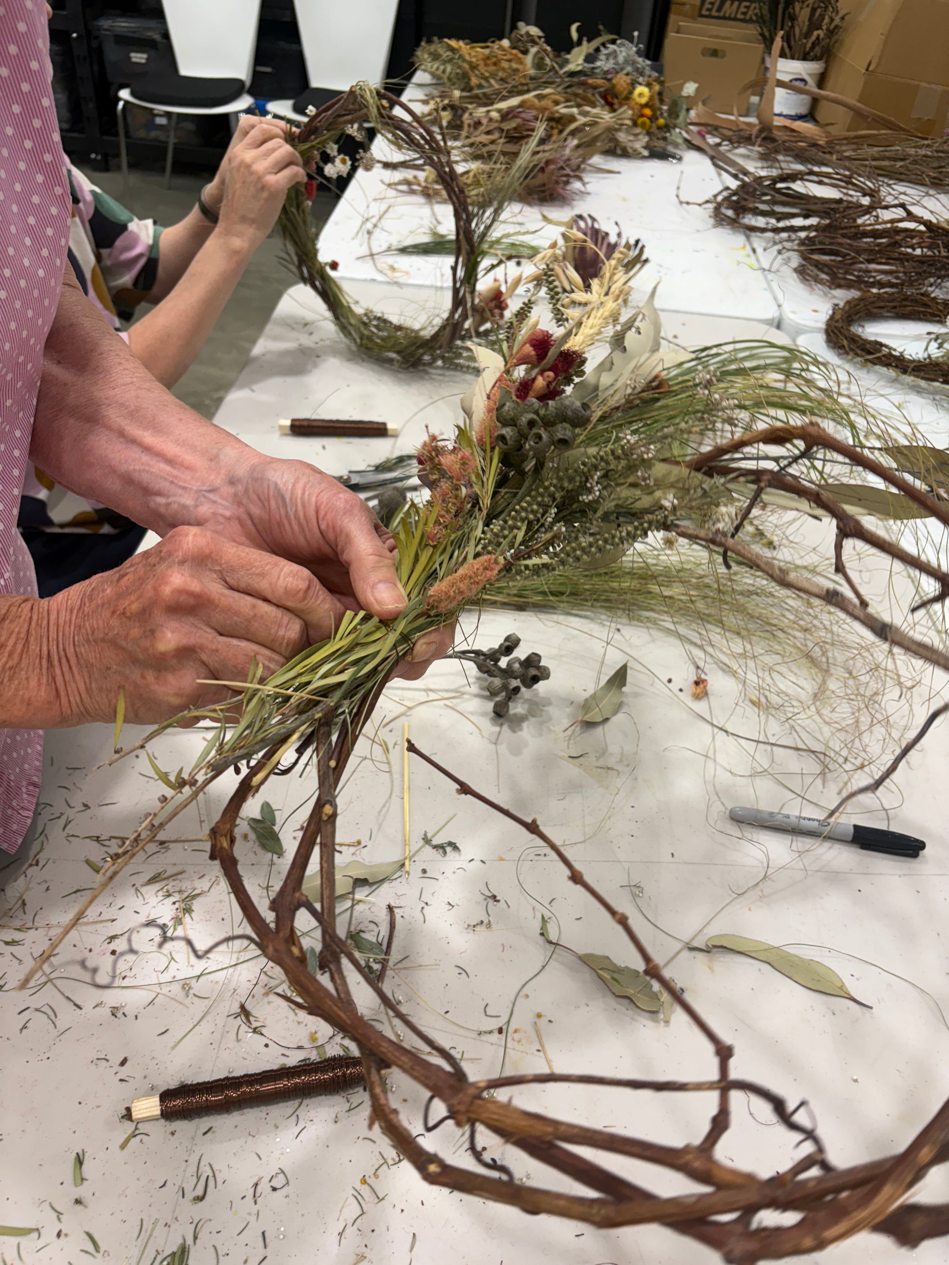 Person crafting a wreath with natural materials on a table.