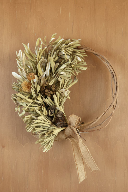 Decorative arrangement of greenery with a gold bow on a wooden surface.